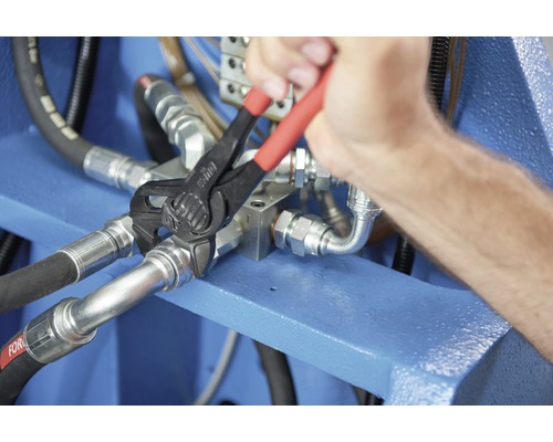 Eine Person benutzt eine Rohrzange an einer Hydraulikverbindung.