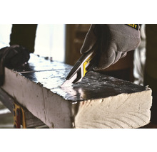 Eine Hand mit Schutzhandschuh schneidet mit einem Universalmesser eine Isolierplatte.