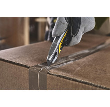 Eine Hand mit Arbeitshandschuh öffnet einen Karton mit einem Stanley Messer.