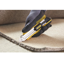 Eine Hand mit Handschuh schneidet Teppich mit einem Stanley Teppichmesser