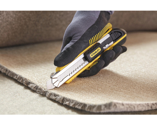 Eine Hand mit Handschuh schneidet Teppich mit einem Stanley Teppichmesser