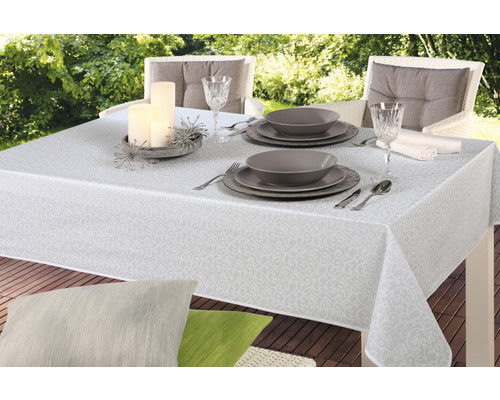 Gedeckter Gartentisch mit weißer Tischdecke mit Muster, Geschirr, Gläsern und Kerzen