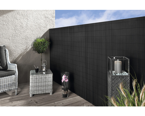 Szene mit schwarzem Sichtschutzzaun, Rattansessel, Rattantisch und Dekoration auf einer Terrasse.