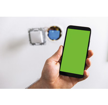 Hand hält Smartphone vor einer unvollständigen Wandinstallation