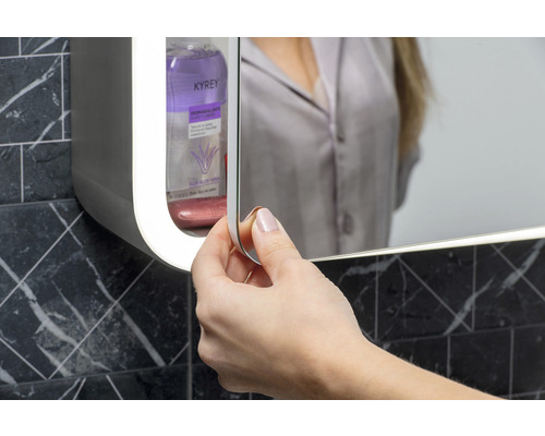 Frau öffnet Spiegelschrank im Badezimmer