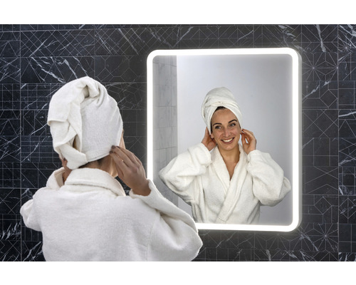 Frau mit Handtuch auf dem Kopf vor beleuchtetem Badezimmerspiegel