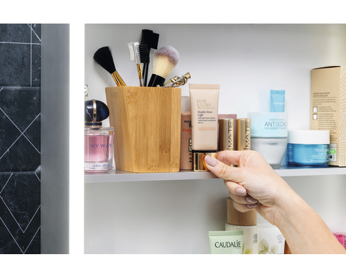 Badezimmerszene mit Kosmetikprodukten, Make-up-Pinsel in einem Behälter und Hand, die eine Dose hält.