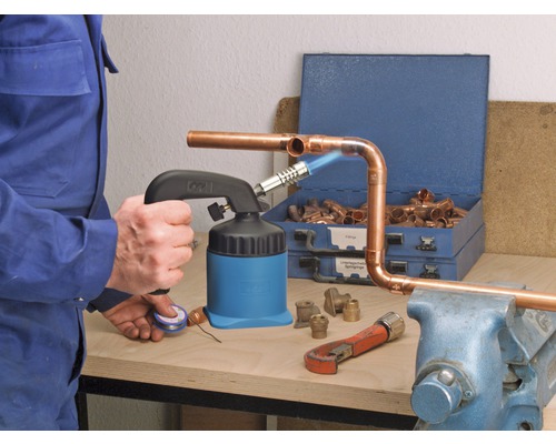 Mann lötet Kupferrohre mit einem Lötbrenner, Armaturen und Werkzeugen auf einer Werkbank
