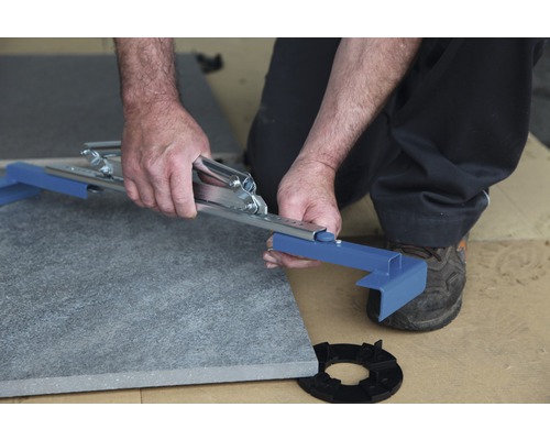 Mann schneidet Steinplatte mit Werkzeug auf Unterkonstruktion.