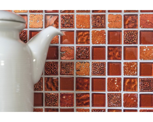 Detailaufnahme einer Wand mit Mosaikfliesen und einer weißen Kanne.