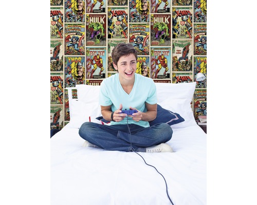 Jugendlicher sitzt mit Videospiel-Controller auf einem Bett vor einer Comic-Tapete