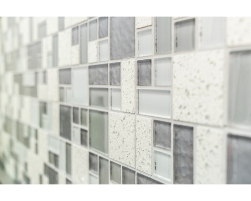Nahaufnahme einer Wand mit Mosaikfliesen in unterschiedlichen Grautönen und Texturen.