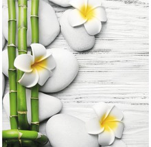Dekorative Anordnung mit Bambusstäben, weißen Steinen und Frangipani Blüten auf einem Holztisch.