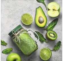 Glas mit grünem Smoothie umgeben von Apfel, Avocado, Limette, Kiwi und Spinatblättern