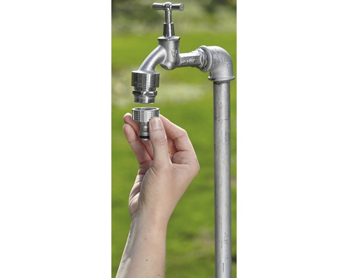 Eine Hand montiert einen Schlauchverbinder an einen Wasserhahn im Garten.