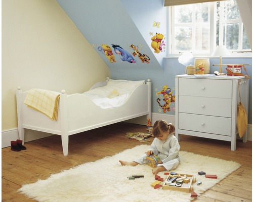 Kinderzimmer mit Wandtattoos, Bett, Kommode und spielendem Kind auf einem Teppich
