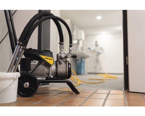 Farbspritzgerät im Einsatz mit Person in Schutzkleidung im Hintergrund