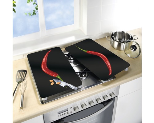 Zwei Herdabdeckplatten mit Chili-Motiv auf einem Herd, mit Kochutensilien und einem Kochtopf in der Nähe.