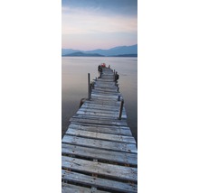 Ein langer, alter Holzsteg führt in ein Gewässer mit Bergen im Hintergrund.