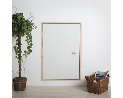 Wand mit Revisionsklappe und Holzrahmen neben einer Kunstpflanze im Topf und einem Korb