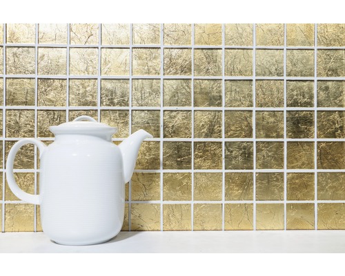 Goldfarbene Mosaikfliesen im Hintergrund mit einer weißen Teekanne im Vordergrund