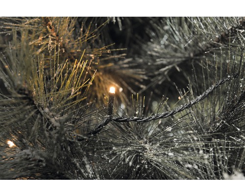 Nahaufnahme einer künstlichen Tanne mit Lichterkette und Schnee