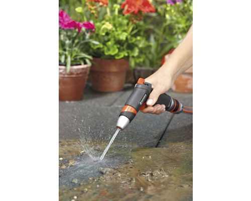 Eine Person benutzt eine Gartenspritze zum Reinigen einer Terrasse vor bepflanzten Töpfen.