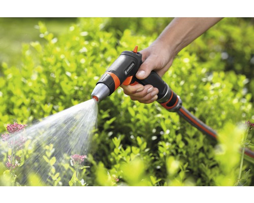 Eine Hand hält eine Gartenspritze der Marke Gardena, aus der Wasser auf Pflanzen spritzt.