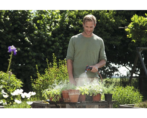 Ein Mann gießt Pflanzen in Töpfen mit einem Gartenschlauch im Garten.