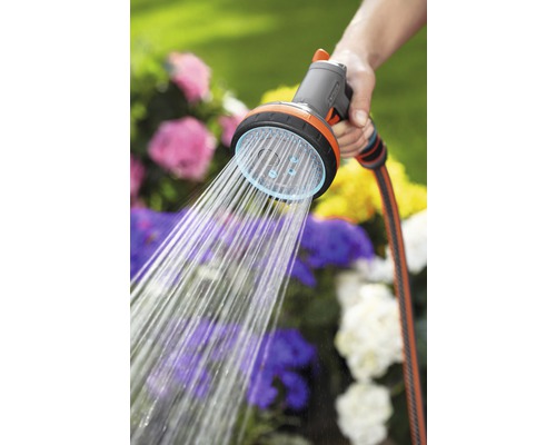 Gartenschlauchbrause mit Wasserstrahl in der Hand vor Blumenbeet