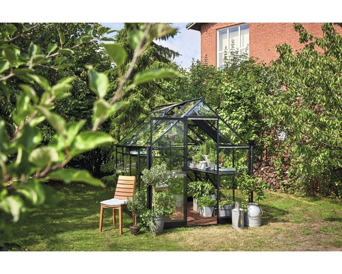 Gewächshaus mit Pflanzen auf einem Rasen neben einem Holzstuhl