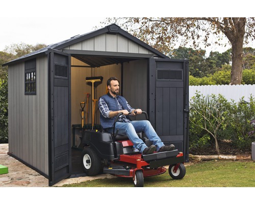 Mann fährt Rasentraktor in ein Gartenhaus zur Rasenpflege.