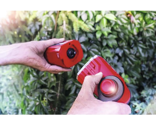 Zwei Hände halten eine elektronische Marderscheuche vor grünem Laub