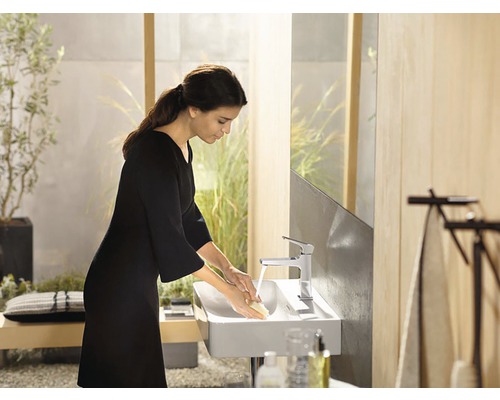 Eine Frau wäscht ihre Hände in einem modernen Badezimmer mit einem Aufsatzwaschbecken und einer Armatur.