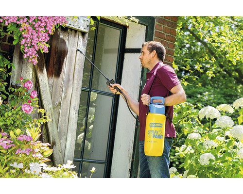 Mann verwendet Gloria Drucksprüher zum Reinigen eines Fensters im Garten