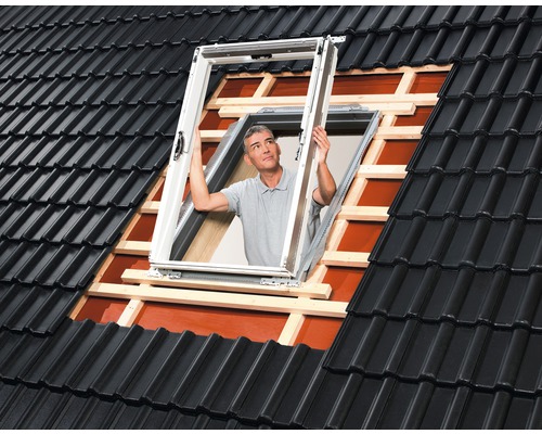 Ein Mann montiert ein Dachfenster in ein Ziegeldach.