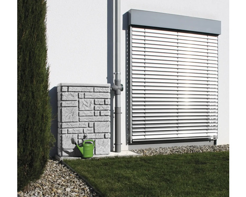 Regenspeicher mit Steinmuster und grüner Gießkanne neben einem Fallrohr vor einer Hauswand