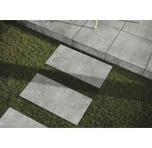 Rechteckige Terrassenplatten aus Stein im Garten auf Rasen verlegt.