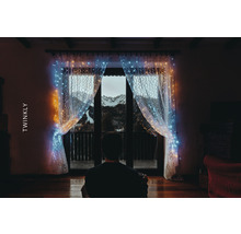Person vor Fenster mit Twinkly Lichterkettenvorhang und Bergblick