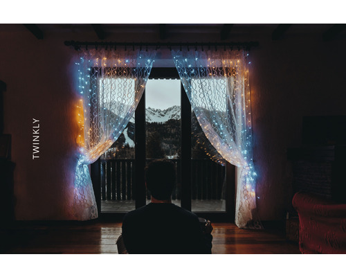 Person vor Fenster mit Twinkly Lichterkettenvorhang und Bergblick