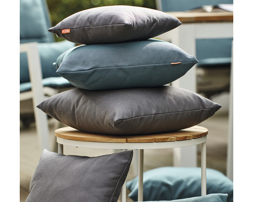 Stapel dekorativer Kissen auf einem Gartentisch.