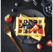 Waffeln mit Blaubeeren und Erdbeeren auf einem Teller, dazu eine Gabel.
