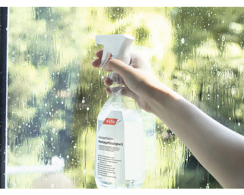 Eine Person sprüht Fensterfolien Montageflüssigkeit auf eine Scheibe.