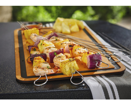 Gegrillte Spieße mit Ananas, Garnelen und roter Zwiebel auf einem Holzbrett.