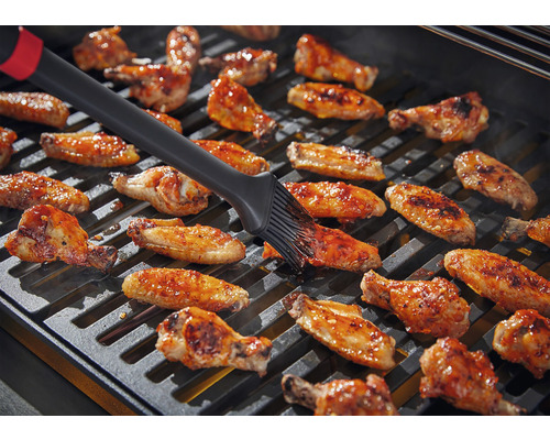 Hähnchenflügel werden auf einem Grill mit einer Bürste bestrichen.