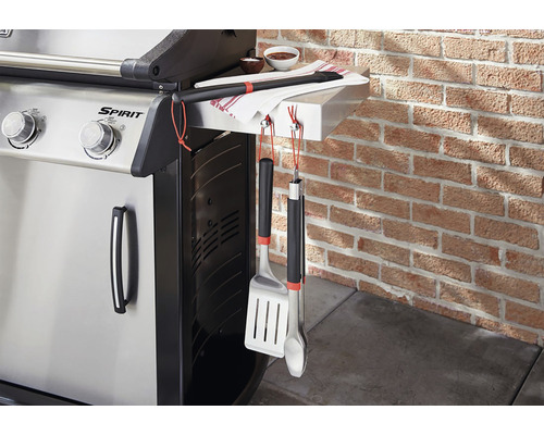Gasgrill mit Grillbesteck und Handtuch an einer Backsteinmauer