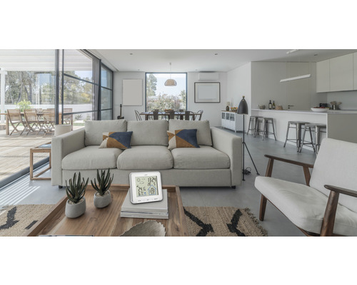 Helles Wohnzimmer mit Sofa, Sesseln, Esstisch und digitalem Thermometer auf einem Couchtisch