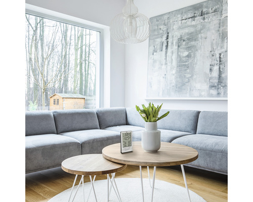 Wohnzimmer mit grauer Couchgarnitur, runden Tischen und digitaler Wetterstation