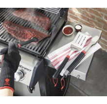 Zubereitung von Speisen auf einem Grill mit Grillbesteck und hitzebeständigen Handschuhen.