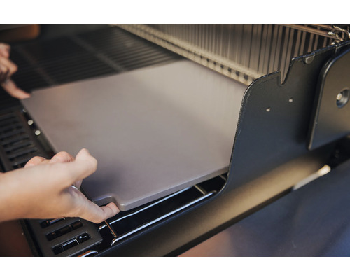 Eine Person platziert einen Pizzastein in einen Grill.